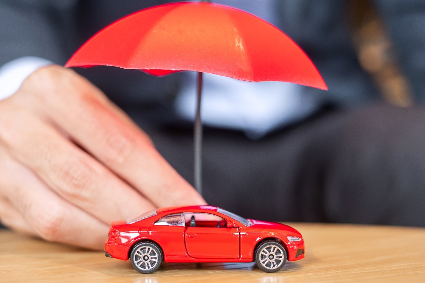 Red toy car under a red umbrella, meant to convey how auto insurance covers damages to a car and its occupants. 